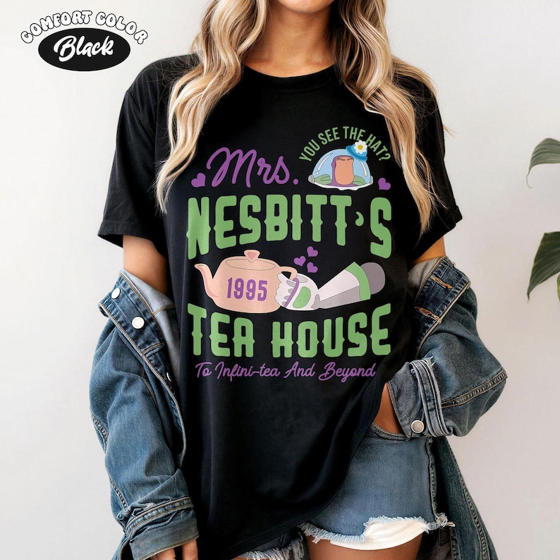 May include: Black Comfort Colors t-shirt with a graphic that reads "Mrs. Nesbitt's Tea House" in green and purple. The design includes a teapot, a teacup, and the text "To Infini-tea And Beyond."