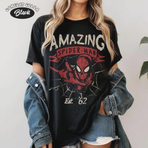 May include: Black t-shirt with a distressed graphic of Spider-Man, the text "AMAZING SPIDER-MAN" in white, and "Est. '62" in white. The shirt has a Comfort Color label.