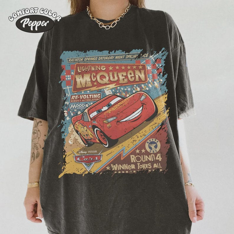 May include: Dark gray t-shirt featuring a graphic of Lightning McQueen from the Disney Pixar Cars movie. The design includes the text "Lightning McQueen" and "Round 4 Winner Takes All". The shirt has a vintage, distressed look.