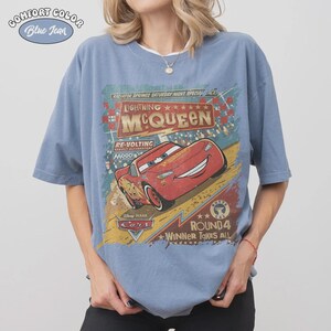 May include: Blue jean Comfort Colors t-shirt featuring a graphic of Lightning McQueen from the Disney Pixar Cars movie. The design includes text that reads "Lightning McQueen", "Round 4", and "Winner Takes All".