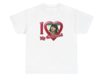 Op de afbeelding: Een wit T-shirt met korte mouwen en een grafisch ontwerp met de tekst I Love My Girlfriend in rode letters. De letter O is vervangen door een rood hartje met daarin een foto van een persoon met donker haar.