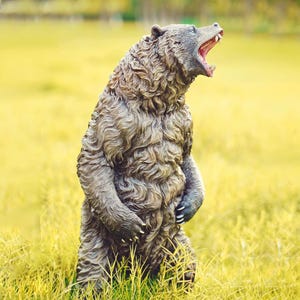 Op de afbeelding: Een gedetailleerd berenbeeld met een open mond, die tanden laat zien. De beer staat rechtop in een veld met hoog, geel gras. Het beeld heeft een getextureerde, bruine vacht.