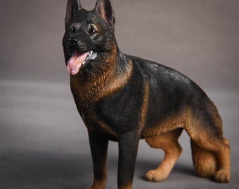 May include: A detailed figurine of a German Shepherd dog, posed in a standing position. The dog has a black and brown coat, with its tongue slightly visible. The figurine is a realistic representation of the breed.