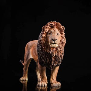 Op de afbeelding: Gedetailleerd beeldje van een leeuw met een bruine manen en een bruin lichaam. De leeuw staat, naar voren gericht, met zijn staart licht gebogen. De zwarte achtergrond benadrukt de details.