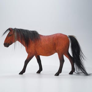 Op de afbeelding: Gedetailleerd beeldje van een paard in een loopstand. Het paard heeft een roodbruin lichaam, zwarte benen en een lange zwarte manen en staart. De staart heeft een wit gedeelte. Het paard staat tegen een effen witte achtergrond.