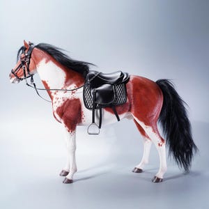 Op de afbeelding: Gedetailleerd model van een paard met een zwart zadel en hoofdstel. Het paard heeft een rood-witte vacht, een zwarte manen en staart. Het zadel heeft zilveren stijgbeugels.