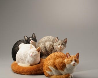 May include: Four sleeping cats figurines, one white, one black and white, one gray and white, and one orange and white. The cats are arranged in a group, with the white cat in the center.