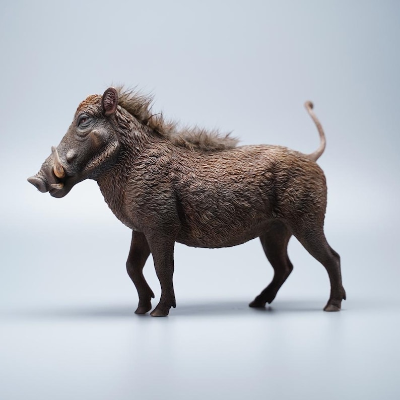 May include: A detailed figurine of a warthog, showcasing a realistic depiction of the animal. The warthog is brown with a textured coat, prominent tusks, and a bristly mane. The figurine is posed in a walking stance.