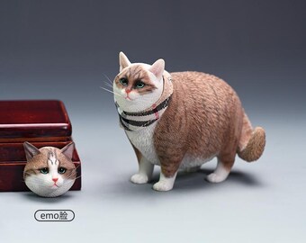 May include: A detailed figurine of a cat with brown and white fur, wearing a striped scarf. The cat has green eyes and a sad expression. A smaller cat head figurine is next to a wooden box. The text "emo face" is below the smaller figurine.