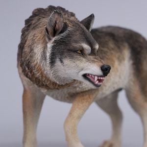 Op de afbeelding: Gedetailleerd beeldje van een wolf, met een realistisch ontwerp. De wolf heeft een mix van bruin, grijs en tan vacht, gele ogen en zichtbare tanden. Het beeldje staat in een dynamische houding, wat beweging suggereert.
