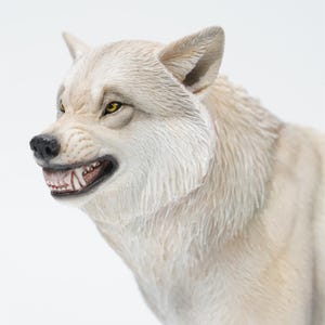 Op de afbeelding: Gedetailleerd beeldje van een grommende wolf. De wolf heeft een lichtgrijze vacht, gele ogen en zichtbare tanden. De sculptuur legt de agressieve uitdrukking van het dier vast.