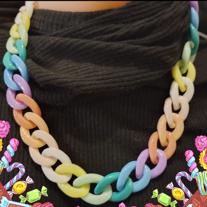 Puede incluir: Un collar llamativo con eslabones grandes de colores pastel. La cadena est&aacute; formada por eslabones de forma ovalada en tonos de blanco, amarillo, naranja, rosa, morado, azul y verde. El collar se muestra sobre un fondo oscuro. La cadena es un accesorio de moda audaz.