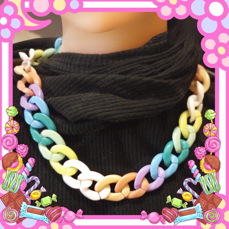 Puede incluir: Un collar de cadena grueso y colorido con eslabones grandes y ovalados. El collar presenta una variedad de colores pastel, incluyendo rosa, azul, verde, amarillo y blanco. El collar se usa sobre un fondo negro.