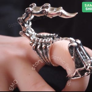 May include: A silver skeletal hand ring with articulated fingers. The ring is designed to fit on multiple fingers.