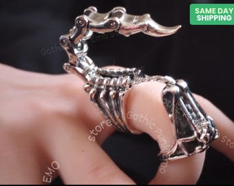 May include: A silver skeletal hand ring with articulated fingers. The ring is designed to fit on multiple fingers.