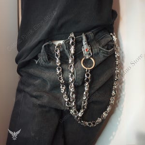 May include: A silver-toned wallet chain with skull and dragon head details. The chain is attached to a belt loop with a dragon head clasp featuring a red gem. The chain is made of multiple skull links.