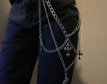 May include: Silver-colored chain belt with multiple strands and decorative cross pendants. The belt is designed to hang from the waist and features various chain styles. The image shows the belt against a dark background, highlighting its metallic shine.