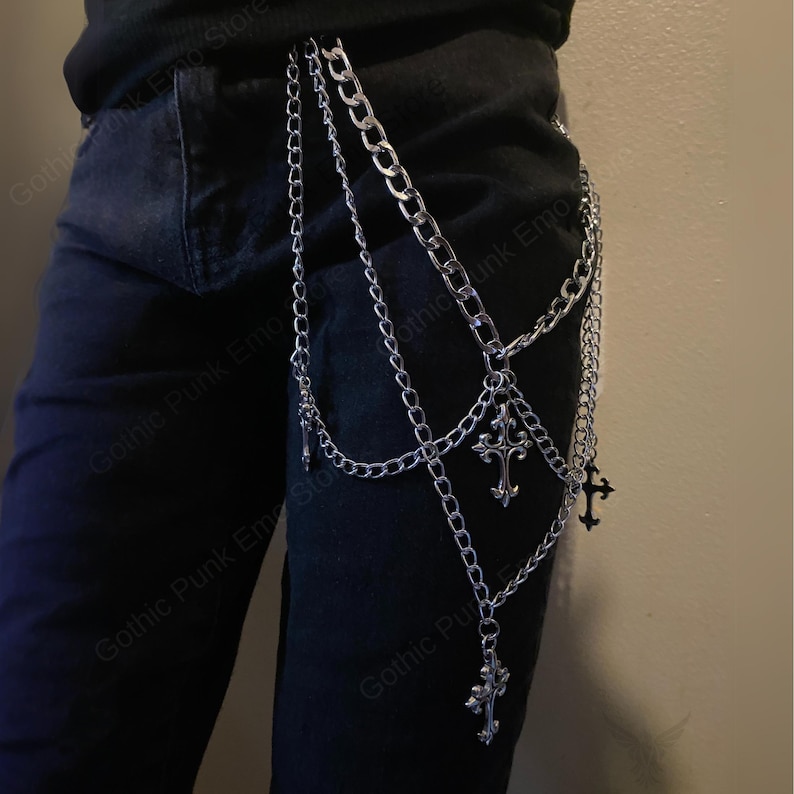 May include: Silver-colored chain belt with multiple strands and decorative cross pendants. The belt is designed to hang from the waist and features various chain styles. The image shows the belt against a dark background, highlighting its metallic shine.