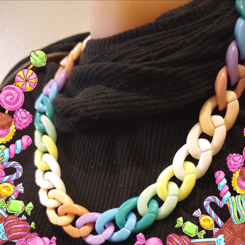 Puede incluir: Un collar grueso y colorido con eslabones grandes y ovalados. El collar presenta una variedad de colores pastel, incluyendo rosa, amarillo, verde, azul y marr&oacute;n. El collar se usa sobre un fondo negro, resaltando los colores vibrantes.