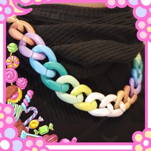 Puede incluir: Un collar de cadena colorido con eslabones grandes e entrelazados. El collar presenta un arco&iacute;ris pastel de colores, incluyendo rosa, morado, azul, verde, amarillo y blanco. El collar se usa sobre un fondo negro.