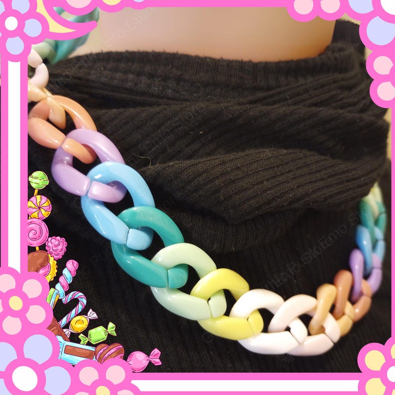 Puede incluir: Un collar de cadena grueso y colorido. El collar presenta eslabones grandes e interconectados en una variedad de colores pastel, incluyendo rosa, morado, azul, verde, amarillo y blanco. El collar se usa sobre un fondo negro.