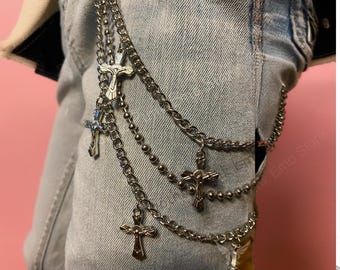 May include: Silver-toned chain belt with multiple strands and dangling crucifix pendants. The belt is layered and attached to light-wash denim jeans. The crucifixes are detailed with a figure of Jesus.