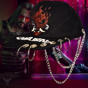 May include: Black baseball cap featuring a red and white Oni mask design and the word "SAMURAI" in white. The cap has silver chain and hoop accents.