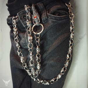 May include: Silver-toned metal wallet chain with skull and dragon head details. The chain is attached to a pair of black jeans. The dragon head has a red gem eye.