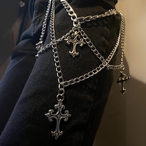 May include: Silver-colored chain body jewelry with multiple strands and decorative cross pendants. The chains are layered and hang from the waist area. The jewelry is designed in a gothic punk style.