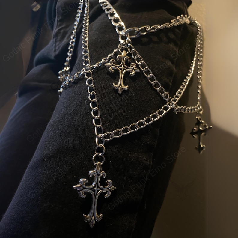 May include: Silver-colored chain body jewelry with multiple strands and decorative cross pendants. The chains are layered and hang from the waist area. The jewelry is designed in a gothic punk style.