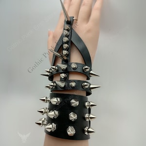 May include: Black leather wrist and finger armor with silver-colored spikes. The armor features multiple bands and a finger loop, all adorned with pointed studs. The design is a bold statement piece.