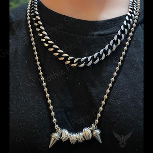 May include: Two silver chains with a black chain layered on top. The bottom chain has a silver spike pendant.