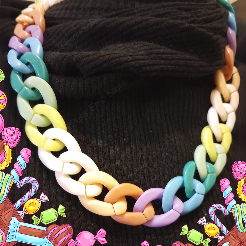 Puede incluir: Un collar de cadena gruesa con eslabones ovalados grandes en tonos pastel como rosa, azul, verde, amarillo y blanco. El collar se usa sobre un fondo negro, creando un fuerte contraste. Esta llamativa pieza es un accesorio de moda llamativo.