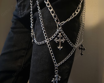 May include: Silver-colored chain leg harness with multiple strands and decorative cross pendants. The harness is designed to be worn on the leg and features a series of interconnected chains. The style is reminiscent of gothic or punk fashion.
