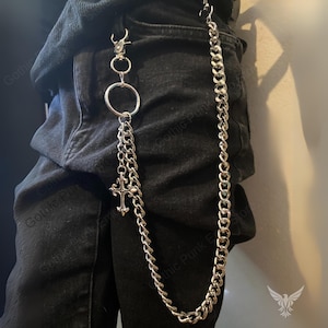 May include: Silver-colored chain accessory with a cross pendant and a large ring. The chain is attached to a clasp and hangs down, designed to be attached to a belt loop. The style is gothic and punk.