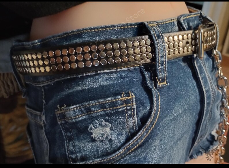 K&ouml;nnte beinhalten: Ein schwarzer Lederg&uuml;rtel mit silbernen Nieten. Der G&uuml;rtel wird &uuml;ber einer blauen Jeans-Shorts getragen.