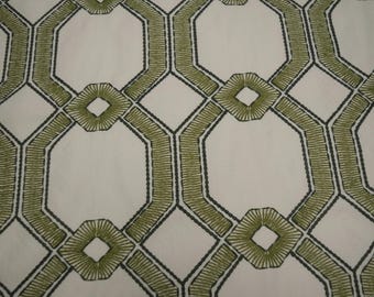 May include: A white fabric featuring a repeating geometric pattern of olive green embroidered octagons and diamonds. The design consists of thick, stitched olive green lines outlined in dark charcoal thread, creating a structured lattice effect.