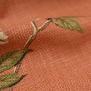 Puede incluir: Primer plano de una tela de color coral con un sutil patr&oacute;n de cuadr&iacute;cula y un dise&ntilde;o floral con hojas verdes y flores blancas.