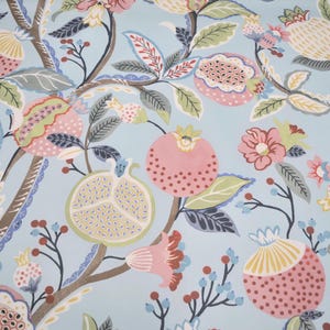May include: A light blue fabric featuring a repeating botanical pattern of stylized pomegranates, flowers, and leaves in shades of pink, green, yellow, and brown. The design includes both whole and halved pomegranates with visible seeds.