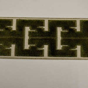 May include: A decorative trim with a geometric pattern. The trim features a dark green, textured design against a light beige background. The pattern is a repeating series of interlocking shapes. A ruler is visible on the right side of the image.