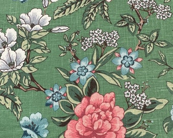 May include: Close-up of a green floral fabric featuring a repeating pattern of large pink, blue, and white flowers. The flowers are surrounded by green leaves and brown branches. The fabric has a textured appearance.