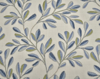 May include: A cream-colored fabric featuring an embroidered botanical pattern of repeating leafy branches. The leaves are stitched in varying shades of blue, light blue, and lime green, creating a textured, repeating design across the surface.