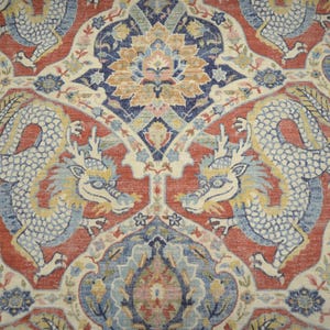 May include: Close-up of a patterned rug featuring two stylized dragons facing each other. The rug has a red background with cream, blue, and yellow accents. The dragons are white with blue and yellow details.