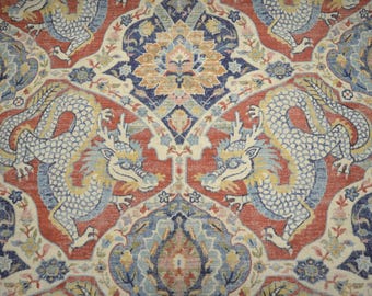 May include: Close-up of a patterned rug featuring two stylized dragons facing each other. The rug has a red background with cream, blue, and yellow accents. The dragons are white with blue and yellow details.