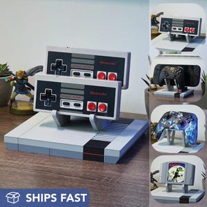 May include: A grey and black Nintendo Entertainment System (NES) console with two controllers. The controllers are grey with black buttons and the Nintendo logo. The image also shows other gaming controllers and a game cartridge.