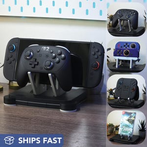 May include: A black gaming console stand with a controller and a screen. The stand has a rectangular base and supports the console and controller. The image also shows other gaming controllers and a game cartridge. The text "SHIPS FAST" is visible.