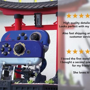 May include: A blue and gold controller stand with a Japanese Torii gate design. The stand holds two controllers, with a detailed design. The controllers are blue with black buttons and gold accents.
