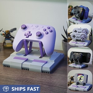 May include: A light purple video game controller resting on a gray and purple stand. The stand is designed to resemble a classic game console. Additional images show other controllers and game console stands.