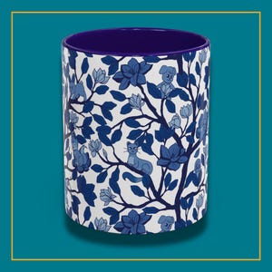 Pu&ograve; includere: Tazza cilindrica in ceramica con un design floreale e animale blu e bianco. L'esterno presenta un motivo di fiori blu, foglie, gatti e cani su sfondo bianco. L'interno della tazza &egrave; di colore blu scuro.