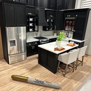 Könnte beinhalten: Miniatur-Küchenset in Schwarz mit einem Kühlschrank aus Edelstahl, weißen Arbeitsplatten und einer Kücheninsel mit zwei weißen Barhockern. Ein goldener Sharpie-Stift befindet sich im Vordergrund.